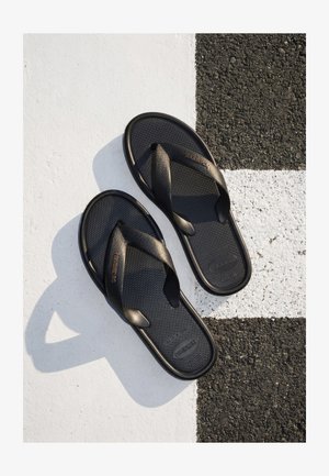 Schwarze Havaianas Flip-Flops auf einer Fläche mit weißen und schwarzen strukturierten geometrischen Mustern.