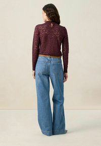 Bordeaux farbenes, langärmliges Oberteil aus Spitze mit Schlüssellochdetails hinten, kombiniert mit hellblauen, weit geschnittenen Jeans im klassischen Fünf-Taschen-Design.