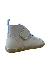 Zapato de cuero beige de caña alta con detalles en azul, una correa de Velcro y suela de goma. Presenta detalles cosidos y una textura suave.