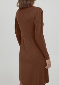 Bruine gebreide jurk met lange mouwen, een aansluitend lijfje en een uitlopende rok. Bevat subtiele pofmouwen en een gladde textuur.
