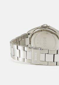 Montre en acier inoxydable argenté avec un bracelet métallique segmenté, dotée d'un fermoir simple et d'une finition lisse et polie.