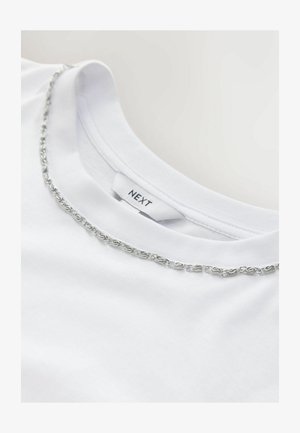 Valge puuvillane t-särk ümarate kaelustega, kaelaääre ääristel hõbedase kett-dekooriga. Sildi peal seisab "NEXT." Pehme tekstuur.