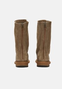 Bottes de cheville en suède marron avec fermeture éclair sur le côté, semelle plate et finition texturée naturelle. Coutures apparentes et détail de couture au dos.