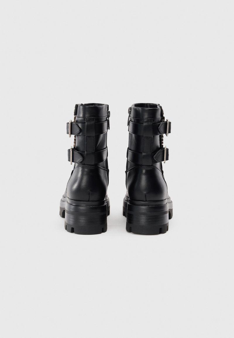Botas de tobillo de cuero negro con suela gruesa, dos correas ajustables con hebillas metálicas y un acabado texturizado.