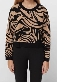 Wełniany sweter z okrągłym dekoltem, z tanowym i czarnym abstrakcyjnym wzorem falistym, długimi rękawami i skróconym dołem. Wykonany z miękkiego materiału.