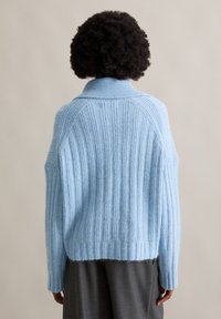 Hellblau gestrickter Pullover mit hohem Kragen und langen Ärmeln, ausgestattet mit einer weichen Textur und einer lockeren Passform. Endet auf Taillenhöhe.