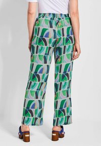 Vloeibare, gepatternde broeken met groene, blauwe en zwarte geometrische ontwerpen. Elastische tailleband en brede pijpen. Gedragen met blauwe hakken.