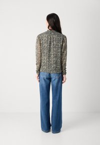 Bluză cu mânecă lungă, cu un model floral în nuanțe de negru și crem, având un guler înalt și mâneci bufante, asortată cu blugi din denim albastru cu picioare largi.