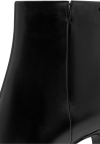Gros plan d'une bottine en cuir noir lisse avec fermeture éclair latérale et petit talon.