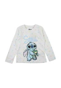 Chemise blanche à manches longues avec des pois colorés ; elle présente un personnage de dessin animé tenant une grenouille, avec "Stitch" imprimé en dessous en lettres pastel.