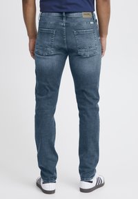 Mörkblå denimjeans för män med slim fit, med bakfickor och en etikett på midjebandet. Slät textur och minimal blekning.