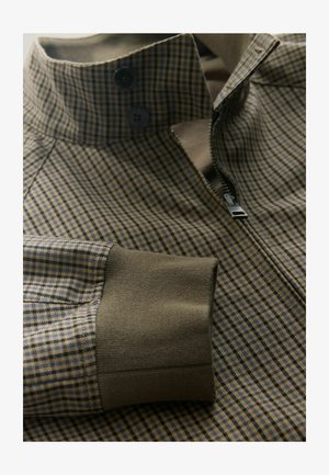 Košeľová bunda s károvaným vzorom v hnedej a modrej farbe, s vysokým golierom, zapínaním na zips a kontrastnými manžetami v olivovo zelenej farbe.