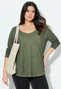 Olijfgroene blouse met lange mouwen, gemaakt van zachte stof, met een ronde halslijn en een ontspannen pasvorm, gecombineerd met een lichtbeige tote bag.