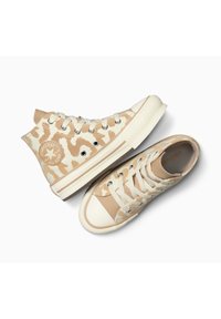 Las zapatillas altas y bajas de lona beige presentan un patrón de camuflaje, ojales de metal y una clásica punta de goma. Acabado suave y texturizado.