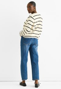 Maglione a righe fuzzy crema con linee nere, abbinato a jeans dritti in denim blu. Un paio di scarpe basse nere completa l'outfit.