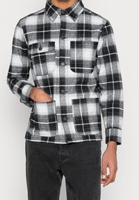 Svart och vit rutigt jacka med krage, två framfickor och knappstängning; tillverkad av ett mjukt, strukturerat tyg.