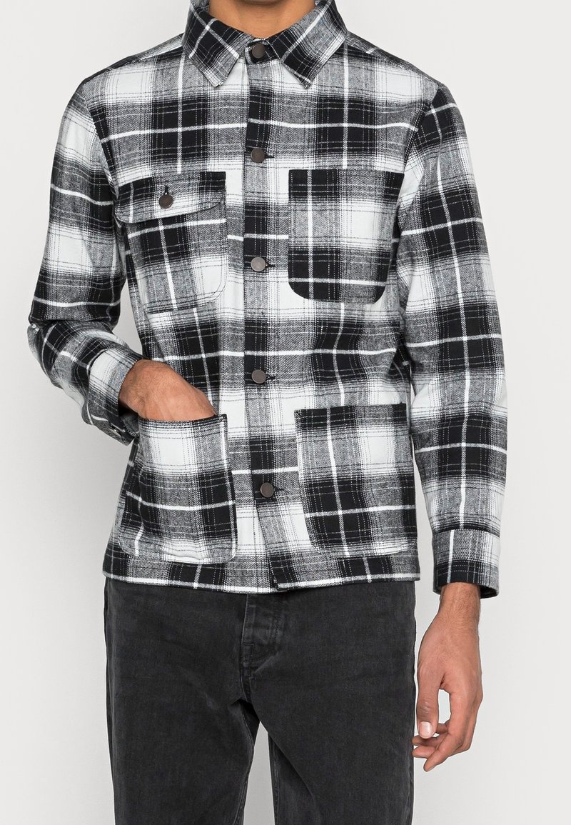 Svart och vit rutigt jacka med krage, två framfickor och knappstängning; tillverkad av ett mjukt, strukturerat tyg.