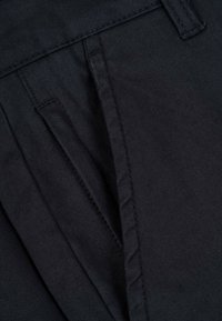 Schwarze Hose aus strukturiertem Stoff mit plissierter Front und geradem Design. Saubere Nähte und eine glatte Oberfläche.