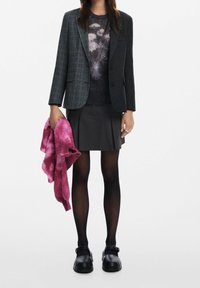 Černý károvaný blazer, šedý pletený svetr s jemným vzorem, plisovaná černá sukna, černé punčocháče, černé dřeváky a růžový tie-dye šál.