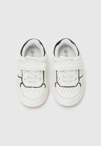 Baskets blanches pour tout-petits avec des contours noirs, des bandes Velcro et des lacets, présentées de dessus sur un fond blanc uni.