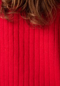 Rode geribbelde trui met verticale strepen, gemaakt van een zachte breimateriaal. De textuur lijkt gezellig met subtiele variaties in dikte.