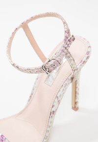 Sandale à talon haut avec fine talonnette stilettos, motif en peau de serpent rose et blanche, et bride de cheville avec boucle en métal.