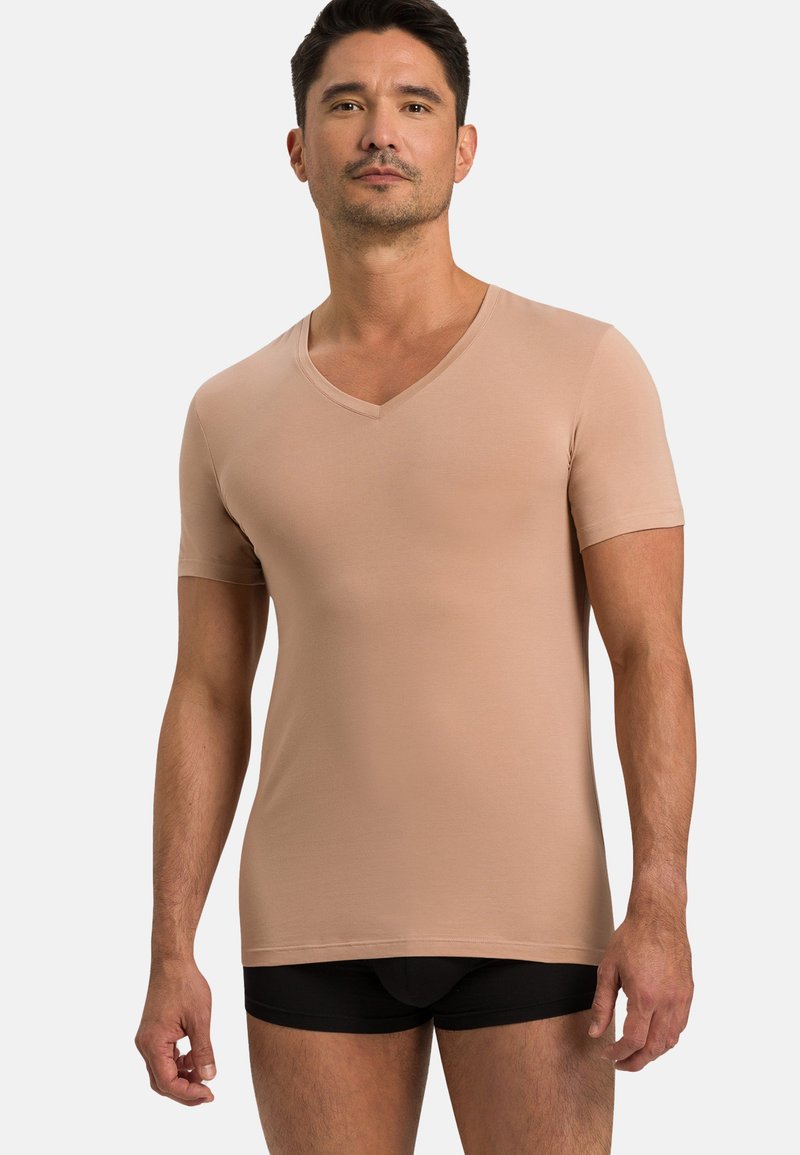 Beżowa koszulka z krótkim rękawem w kształcie litery V, o dopasowanym kroju, wykonana z gładkiego materiału. Połączona z czarnymi dopasowanymi szortami, widocznymi na dolnej krawędzi.