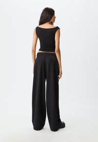 Schwarzes, eng anliegendes Crop-Top mit weitem Ausschnitt, kombiniert mit hoch taillierten, lockeren schwarzen Hosen. Glatter Stoff mit minimalem Detail.