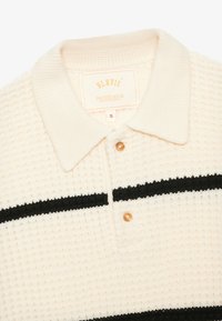 Polo shirt tricotat în crem cu dungi negre. Are guler, placket cu trei nasturi și țesătură texturată. Eticheta de mărime: S.
