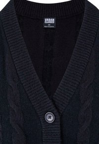 Zwarte gebreide cardigan met een V-hals, geribbelde textuur, kabelaccenten en een enkele knoopsluiting. Etiket leest "Urban Classics" en maat XS.