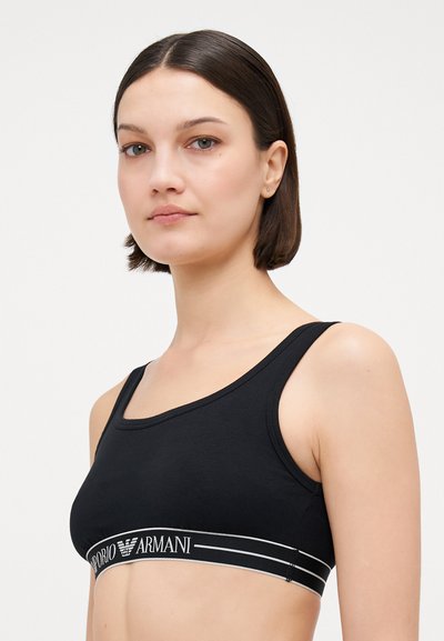 Melna kokvilnas krūšturis ar platām, elastīgām joslām, uz kurām ir baltais "Emporio Armani" logo. Vienkāršs dizains ar noapaļotu dekoltē un biezām siksnām.