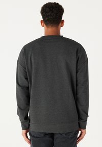 Sudadera gris carbón con manga larga, cuello redondo, corte relajado y puños acanalados. La tela es suave y ligeramente texturada. Sin marca visible.
