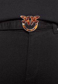 Černý látkový pás má kulatou přezku se dvěma hnědými ptačími akcenty. Přezka je kovová s lesklým povrchem.