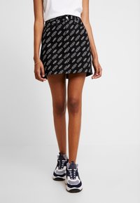 Svart denim minikjol med vit upprepande logotypmönster, rak modell, femficksdesign och framknäppning.