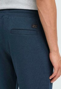 Donkerblauwe joggingbroek van textuurstof, met een achterzak, elastische tailleband en een klein leren label met merkdetails.