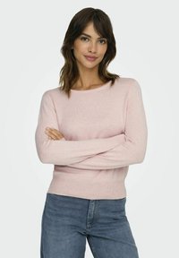 Un pull en tricot rose clair avec des manches longues, un col rond et des poignets côtelés. Associez-le avec un jean bleu. Texture lisse, design simple.