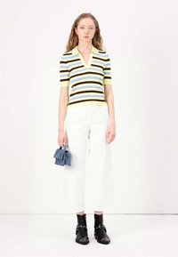 Model má na sebe pruhovaný, krátky rukáv, výstrih do V v žltej, hnedej a modrej farbe, ktorý skombinoval s bielymi širokými džínsami a čiernymi členkovými čižmami.