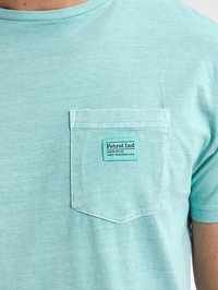 T-shirt in cotone verde chiaro con collo a giro, taschino sul petto, decorato con un'etichetta rettangolare con il nome del marchio e i dettagli.