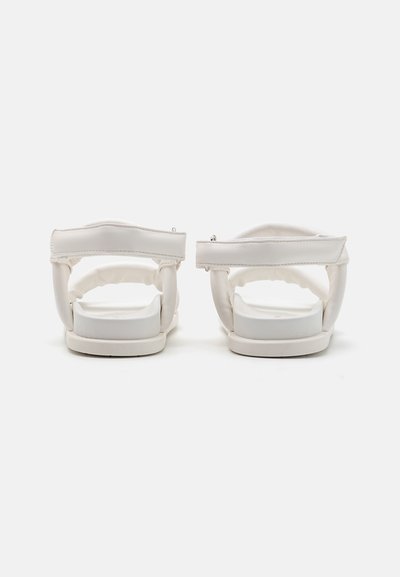 Sandalias blancas con una correa trasera acolchada, suela plana y textura suave. Diseño sencillo con acentos de hardware mínimos.