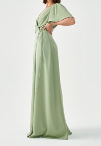 Lång, flytande klänning i ljusgrön satin. V-ringning med korta volangärmar, åtsittande midja med knyt detaljer, och sidoklyvning. Slät textur.