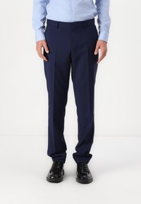 Navy blue tailored pants feature a straight fit, two front pleats, and belt loops, paired with black lace-up shoes.