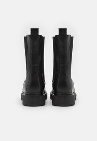 Botas de tornozelo em couro preto com textura lisa, painéis laterais elásticos e sola de borracha resistente. Apresentam um bico arredondado e costura minimalista.
