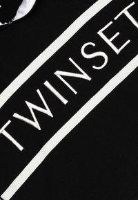 Tessuto nero con il testo bianco ricamato "TWINSET" in evidenza al centro, circondato da due strisce orizzontali bianche. Texture liscia.