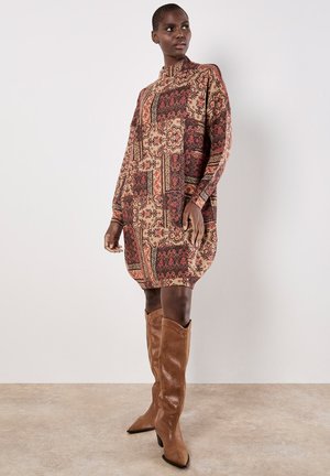 Vestido de manga larga con un diseño estampado en tonos rojos y beiges. Combinado con botas de cuero marrón hasta la rodilla.