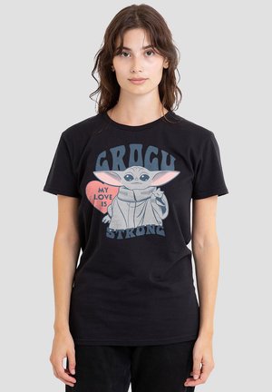Young woman with long brown hair wearing a black t-shirt featuring Baby Yoda and the text "My love is strong, Grogu".
