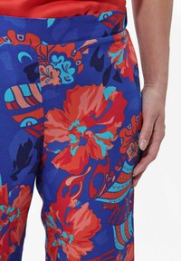 Blaue Hosen mit Blumenmuster, die große rote und türkisfarbene Blumen zeigen, aus glattem Stoff gefertigt und mit einer körpernahen Passform sowie einer Seitentasche.