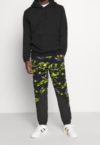 Svart hoodie med framficka, kombinerad med grå och mönstrade joggers med en livlig grön och svart design. Stylar med vita sneakers.