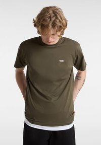 Camiseta de manga corta verde oliva hecha de tela suave, con un pequeño logo blanco de Vans en el lado izquierdo del pecho y un cuello redondeado.