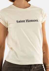T-shirt di cotone color crema con maniche a risvolto, con la scritta "Saint Honoré" in nero sul petto. Texture liscia, vestibilità comoda.