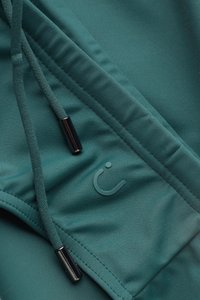 Türkisfarbenes Sportgewebe mit glatter, dehnbarer Textur, ausgestattet mit einem Kordelzug und metallischen Akzenten. Das Markenlogo ist in das Material eingeprägt.